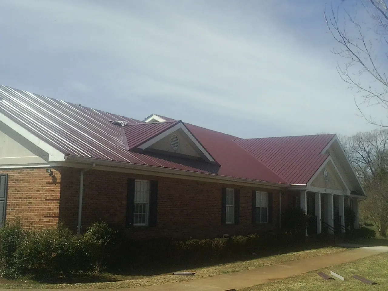 Red metal roof with gabled entries on a long brick building, from a Hail Damage Roof Repair job in Dalton