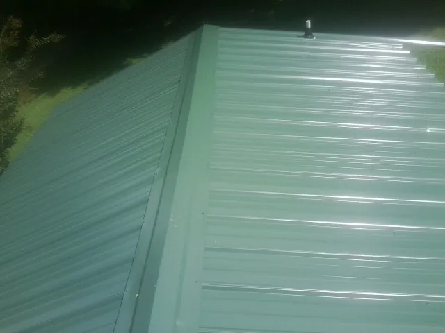 New green metal panels meeting at the ridge of a roof — Flat Roof Repair work by our crew in Dalton